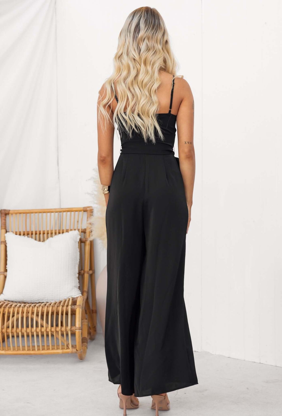 Woman wearing a black Couver jumpsuit with adjustable spaghetti straps, seen from the back.