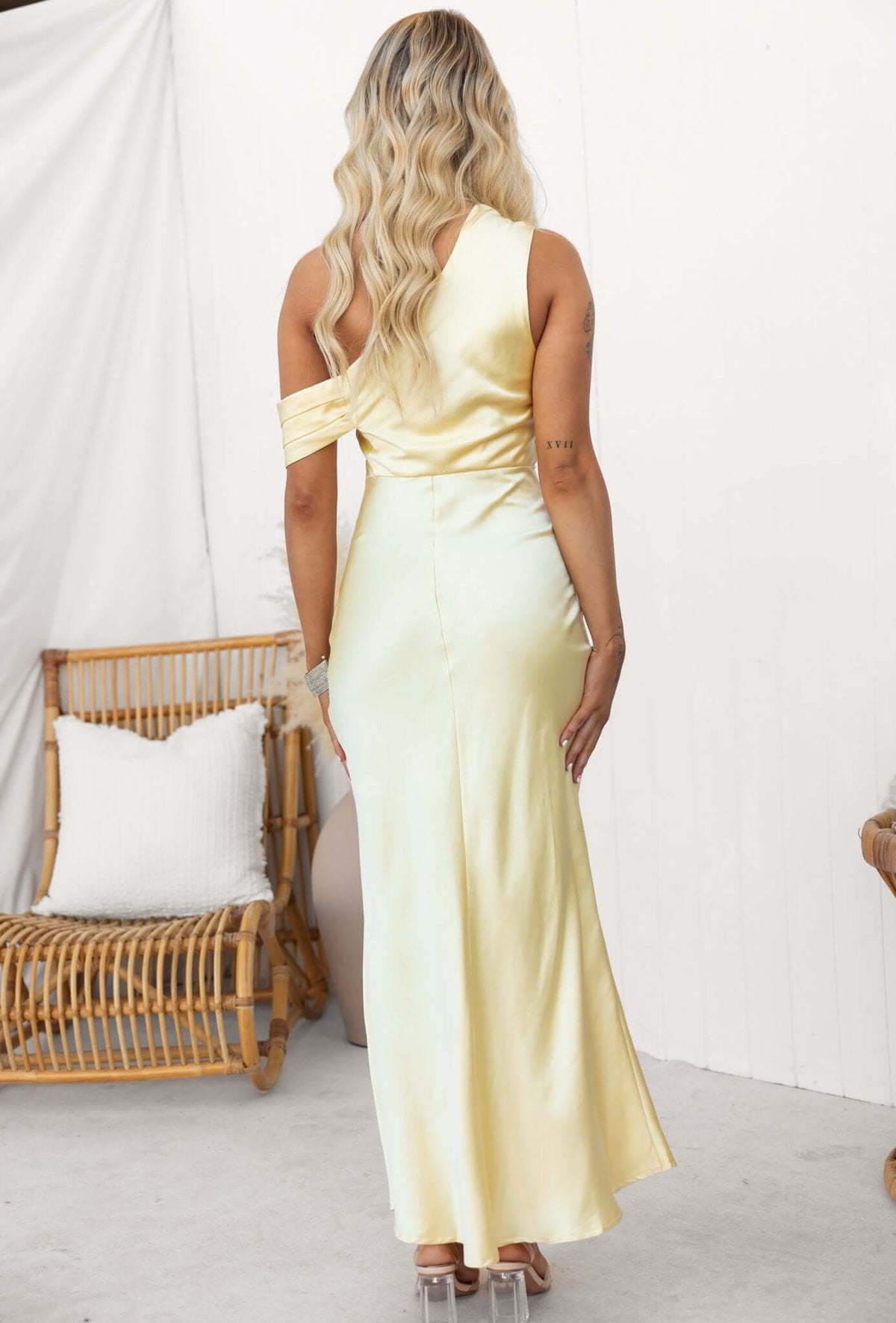 Back view of a woman in a satin off-shoulder yellow maxi dress with a side split and invisible zipper.