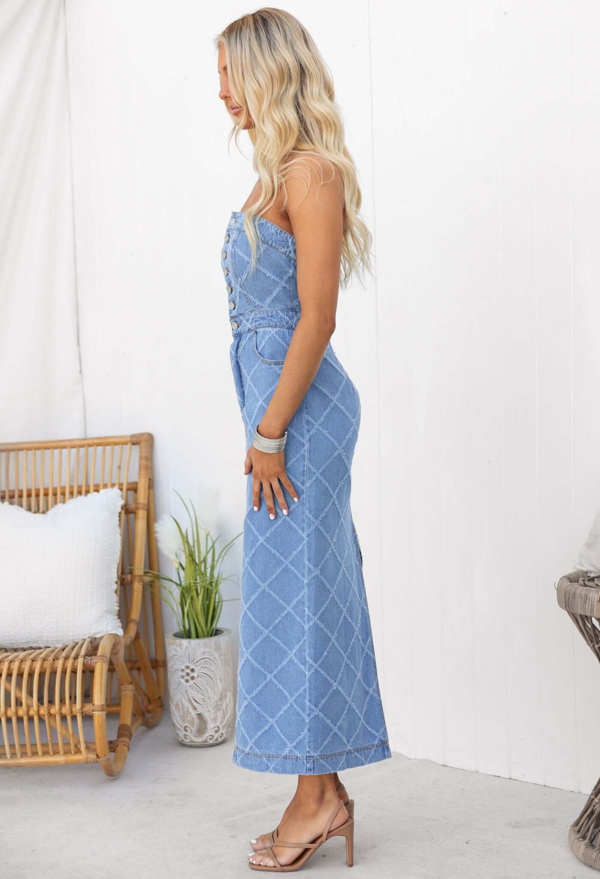 Side view of a woman wearing a strapless denim maxi dress with buttons and pockets, featuring a stylish split at the back.