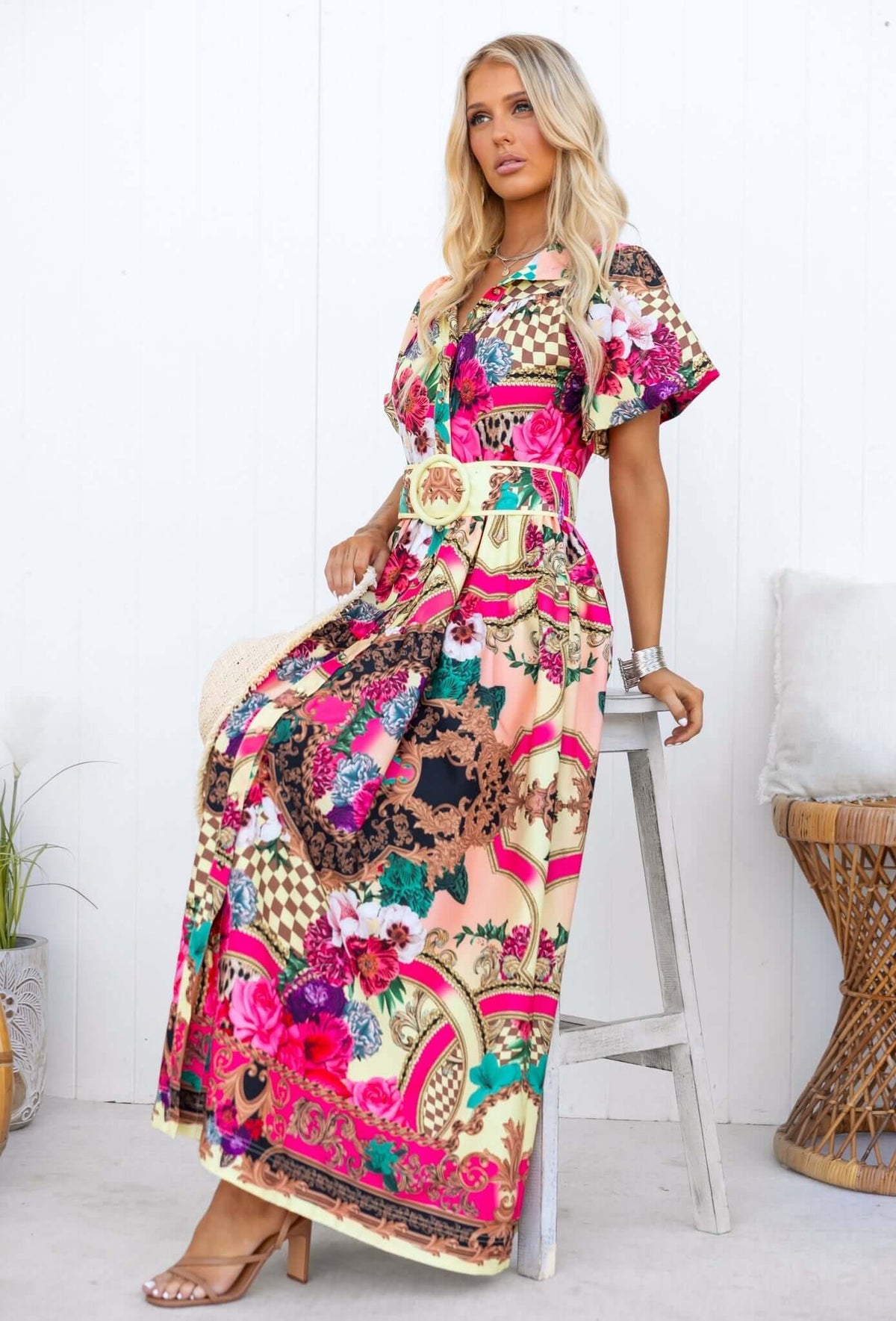 Woman in Palermo Maxi Dress with colorful floral print, removable belt, and relaxed fit, seated on stool.