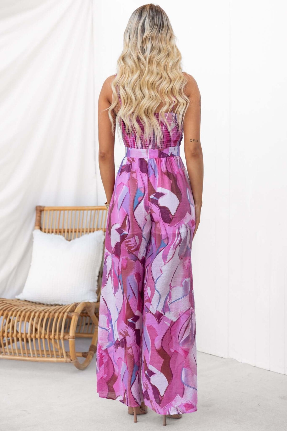 Back view of a model wearing the multi-colour Sun Dazed jumpsuit with adjustable straps and tie at bust.