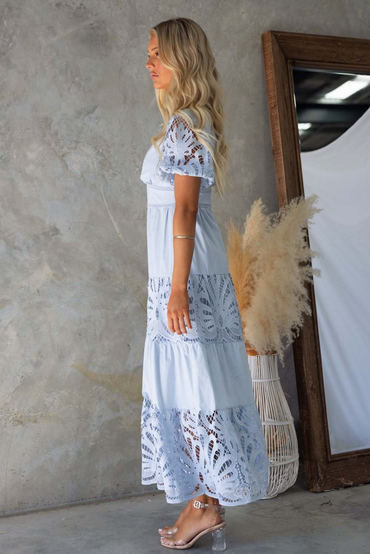 Side view of a model in the Hammond Maxi Dress, showcasing its lace details and tiered skirt, against a textured backdrop.