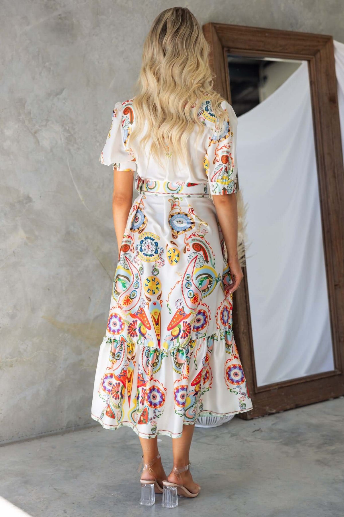 Back view of woman in Kiton maxi dress with colorful print and ruffled hem, styled with a removable belt.