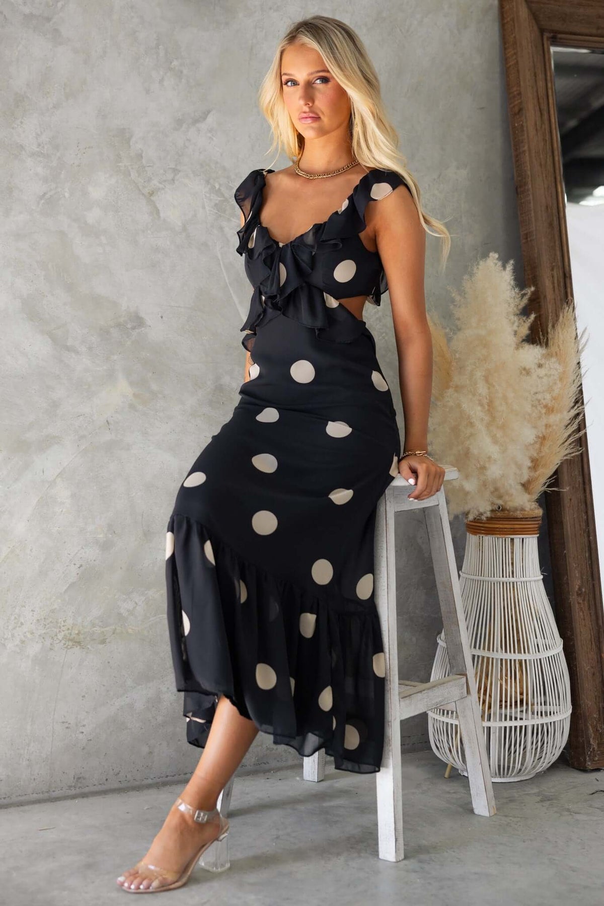 Model wearing a black polka dot maxi dress with ruffled sleeves, styled with a chic hairstyle, against a textured background.