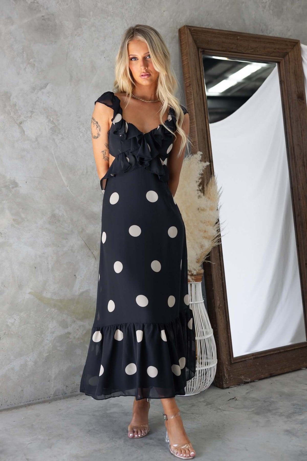 Elegant black polka dot maxi dress with ruffled straps and flared hem, featuring a stylish open back.
