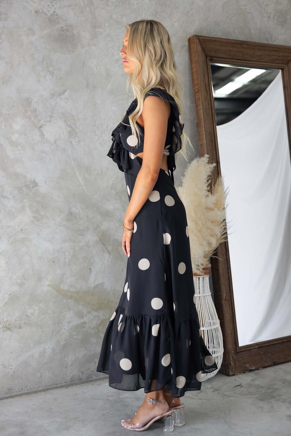 Side view of a woman wearing a black maxi dress with polka dots and ruffles, showcasing elegant design and silhouette.