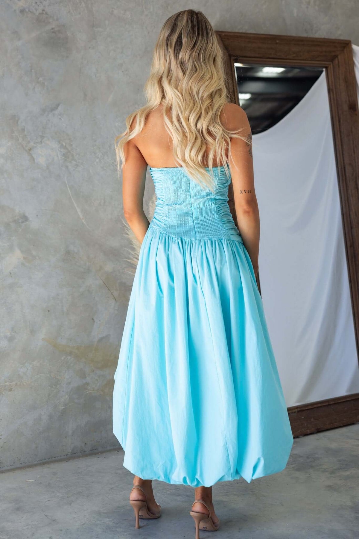 Back view of a strapless light blue Carette midi dress with an asymmetric hemline and elastic back.