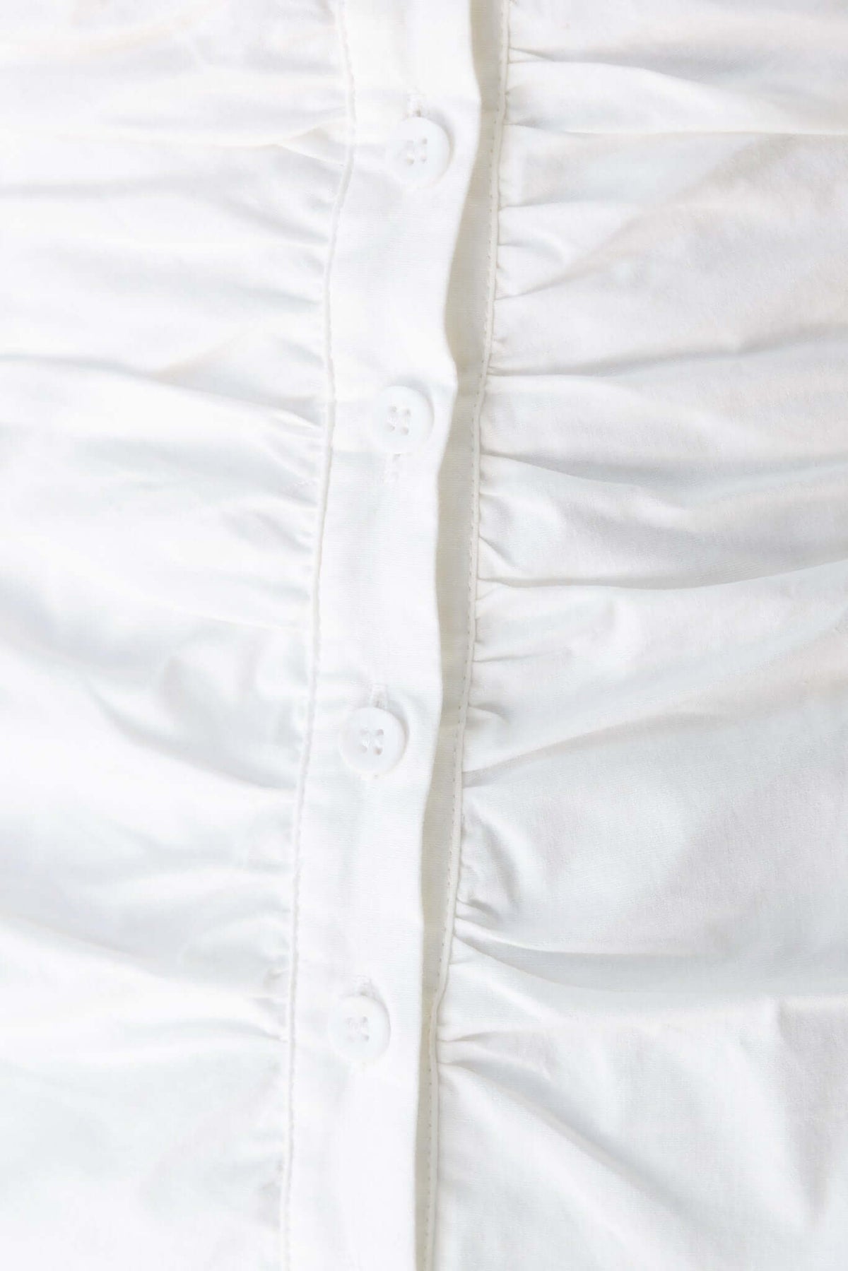 Close-up of the button-down front of the Saint Mini Dress, featuring a white fabric with slight ruching.