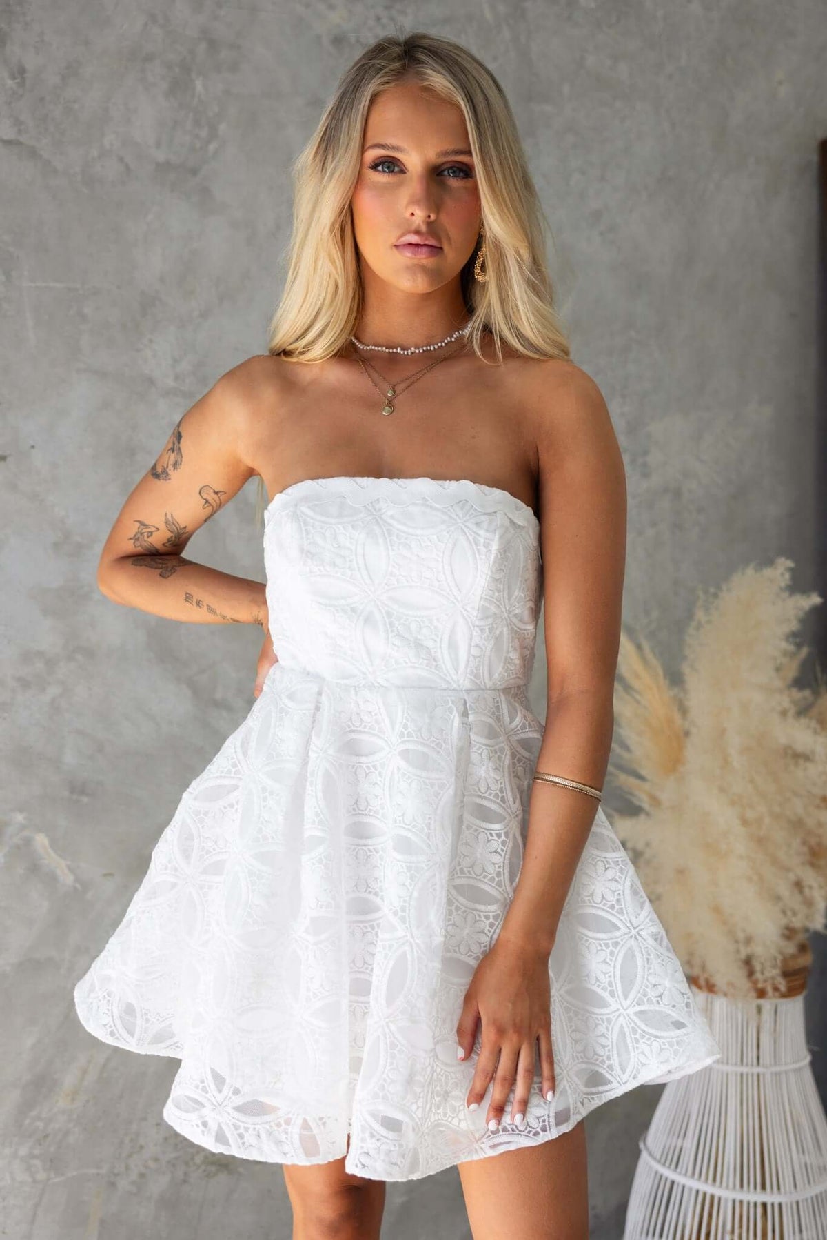 Model wearing a strapless Millicent dress in white lace with a flared skirt, showcasing elegant summer style.