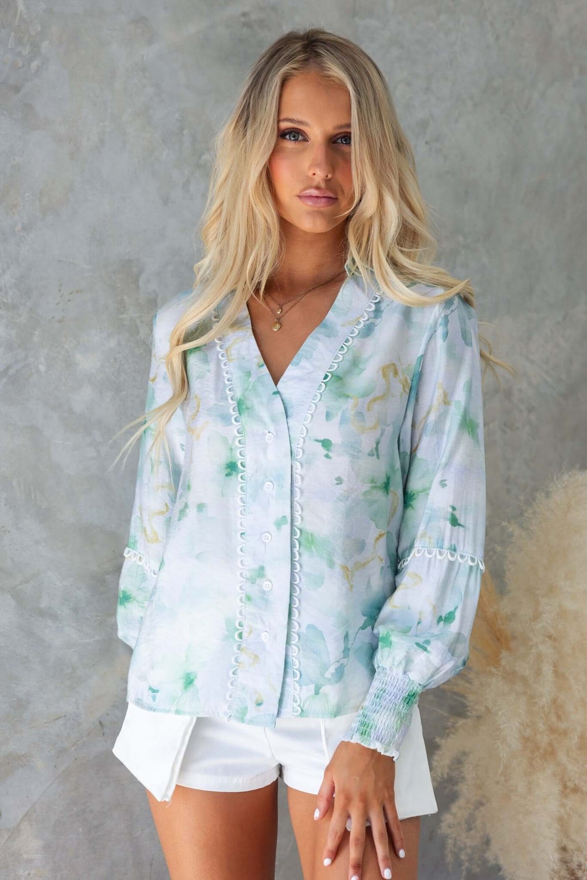 Kellee Shirt in soft blue floral print, featuring a collar, button-up front, and elastic sleeves, worn with white shorts.