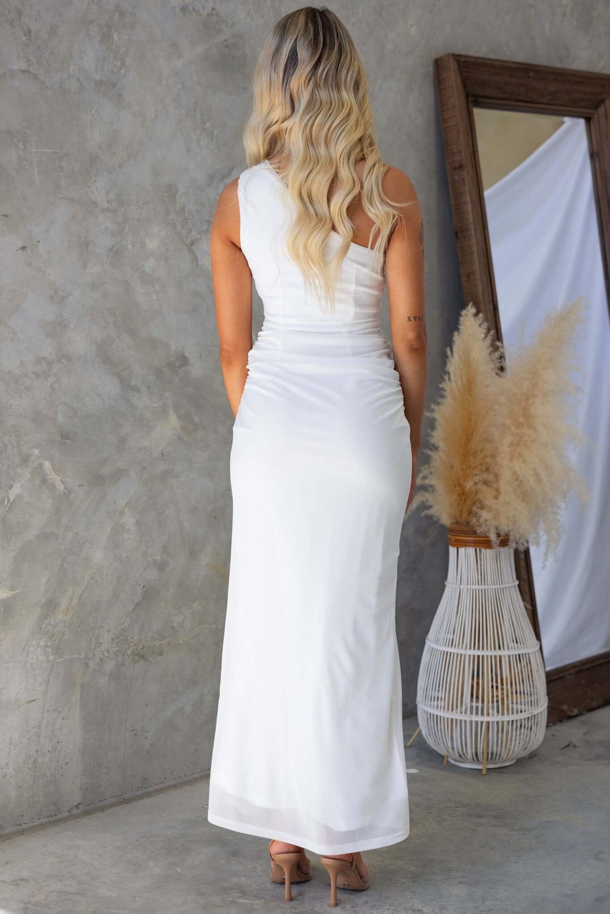 Back view of a woman in a one-shoulder white maxi dress, featuring a sleek design and soft mesh material.