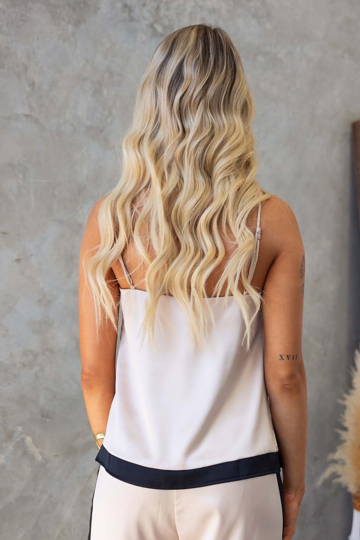 Back view of a woman wearing a tan satin top with adjustable straps and a split at the side.