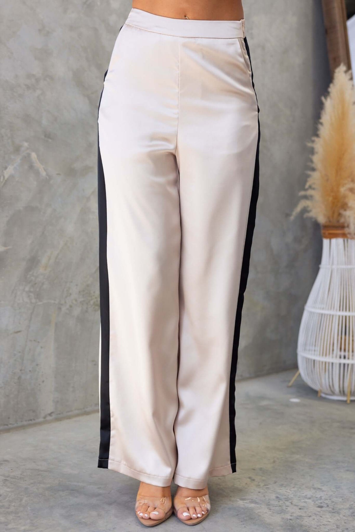 Tanaya Pants in beige with black side stripes, featuring a mid-high waist, pockets, and a satin finish.