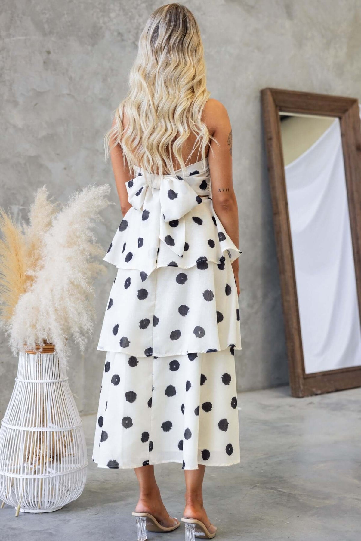 Back view of a Portici midi dress featuring a strapless design, ruffle skirt, and polka dot pattern.