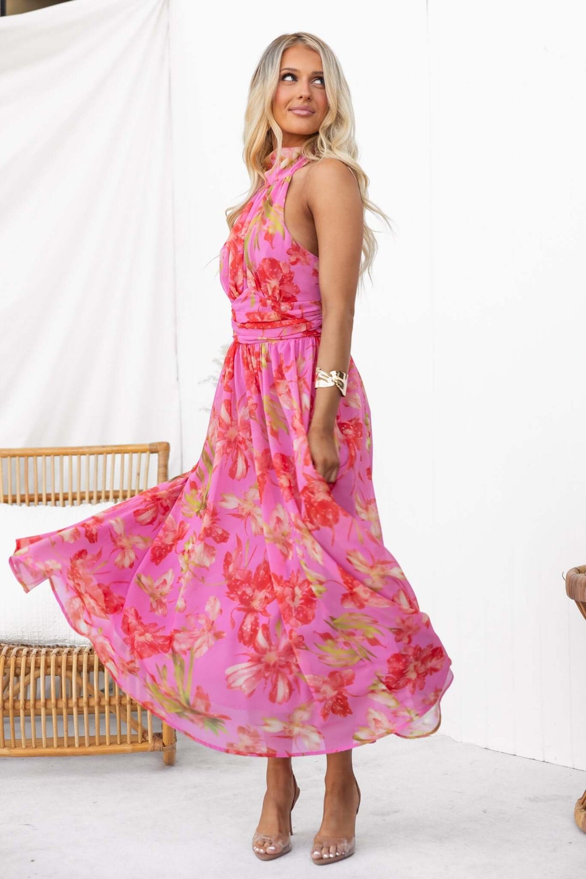 Model twirling in a pink floral Giulianna Maxi Dress with a tie neck and zip back, showcasing a flowy design.