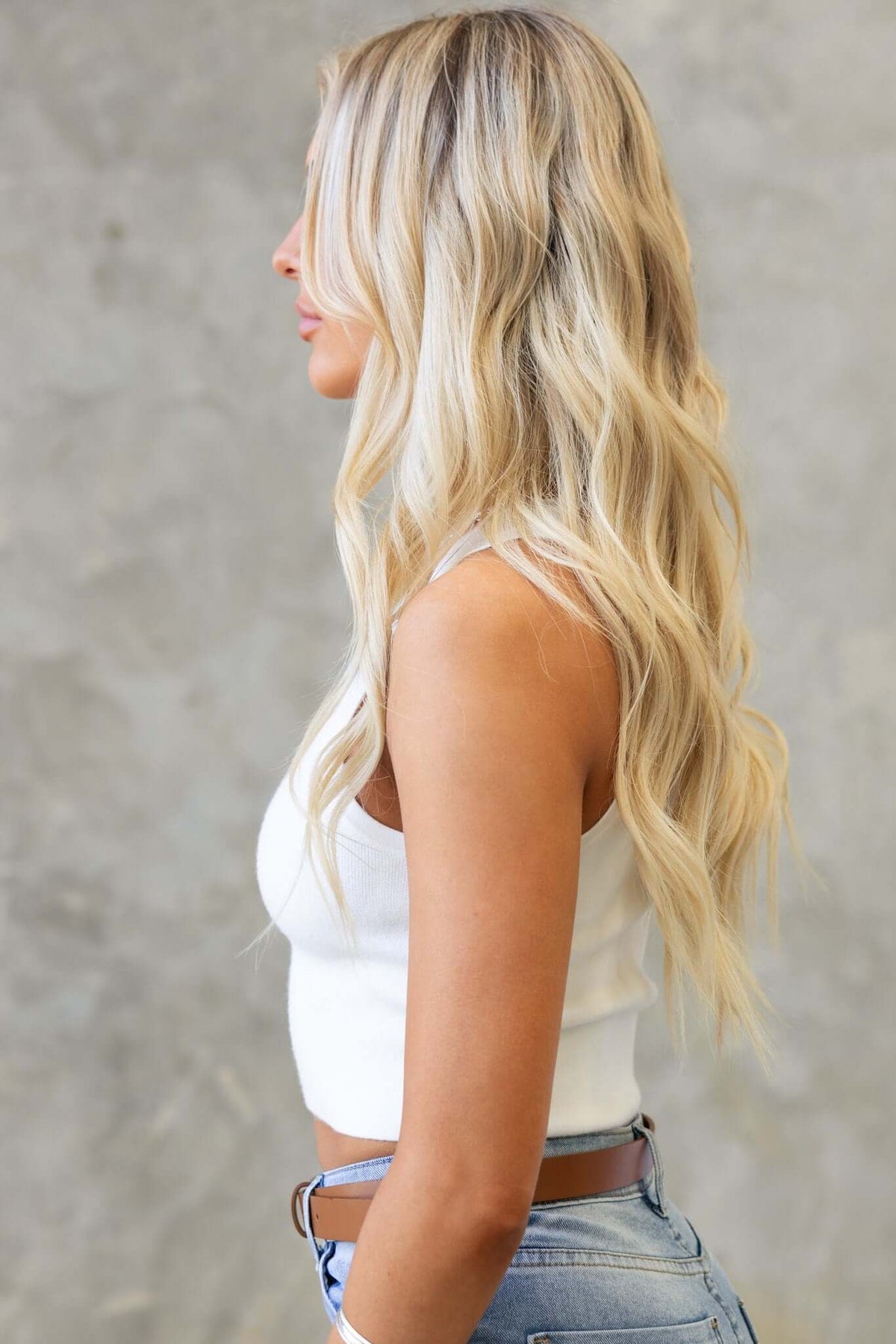 Model in a soft knit white semi-crop top paired with high-waisted denim shorts, showcasing a stylish side profile.