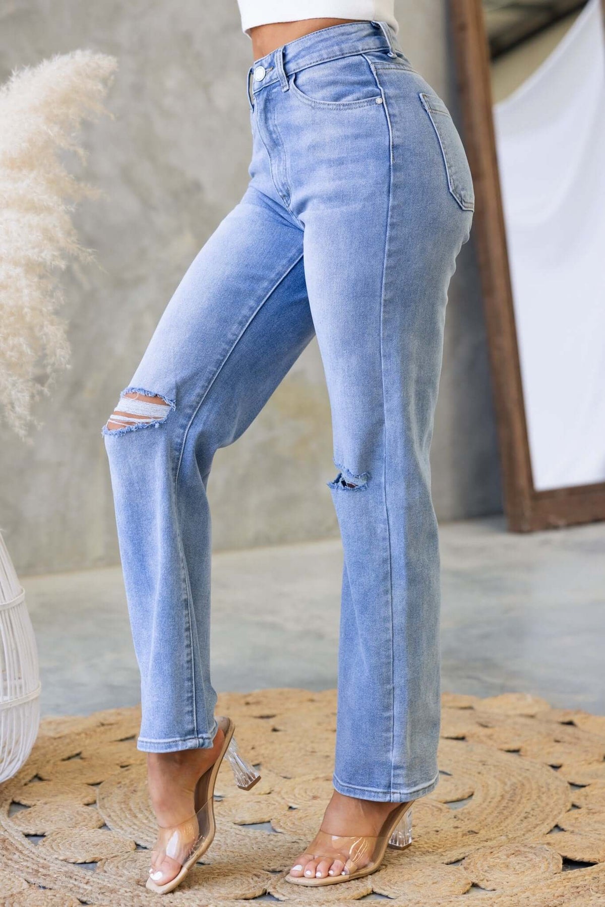 Distressed denim Tekin jeans featuring ripped details and a fitted silhouette, styled with clear heels on a woven rug.