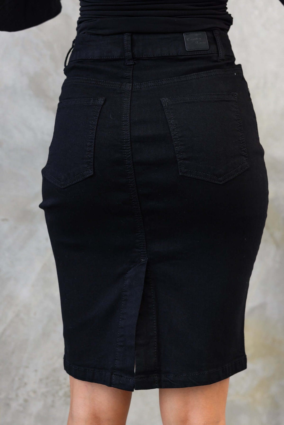 Black denim skirt with mid-high waist, back split, and pockets, showcasing a firm stretch fit.