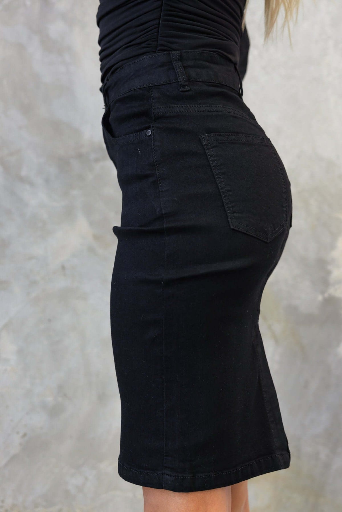 Side view of a black denim skirt featuring mid-high waist fit and back pocket detail.