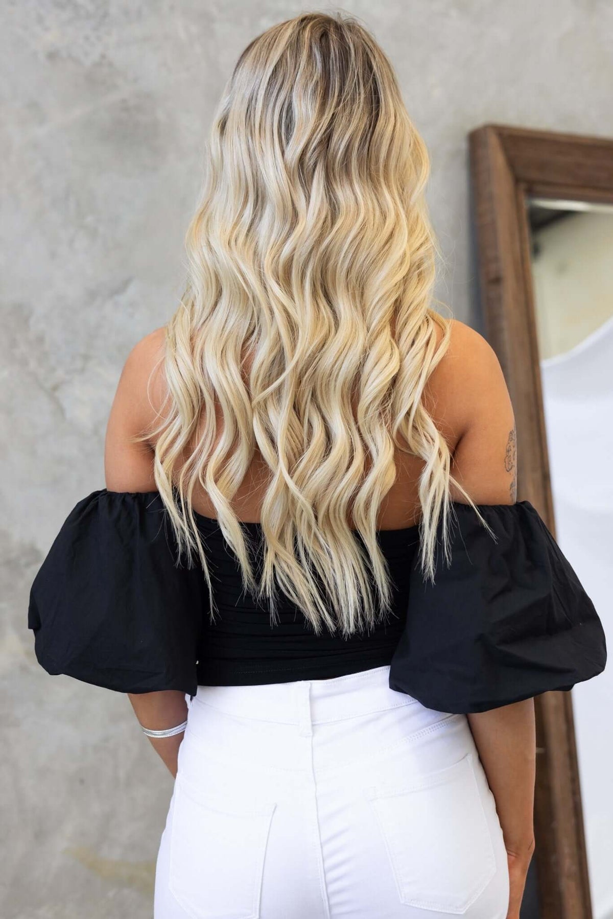 Model wearing Ivita Top, off-shoulder black top with puff sleeves, showcasing long wavy blonde hair.