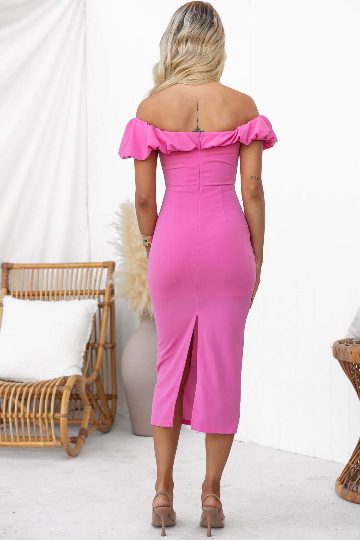 Back view of a pink Stresa Midi Dress with off-shoulder style and back split, showcasing a fitted silhouette.