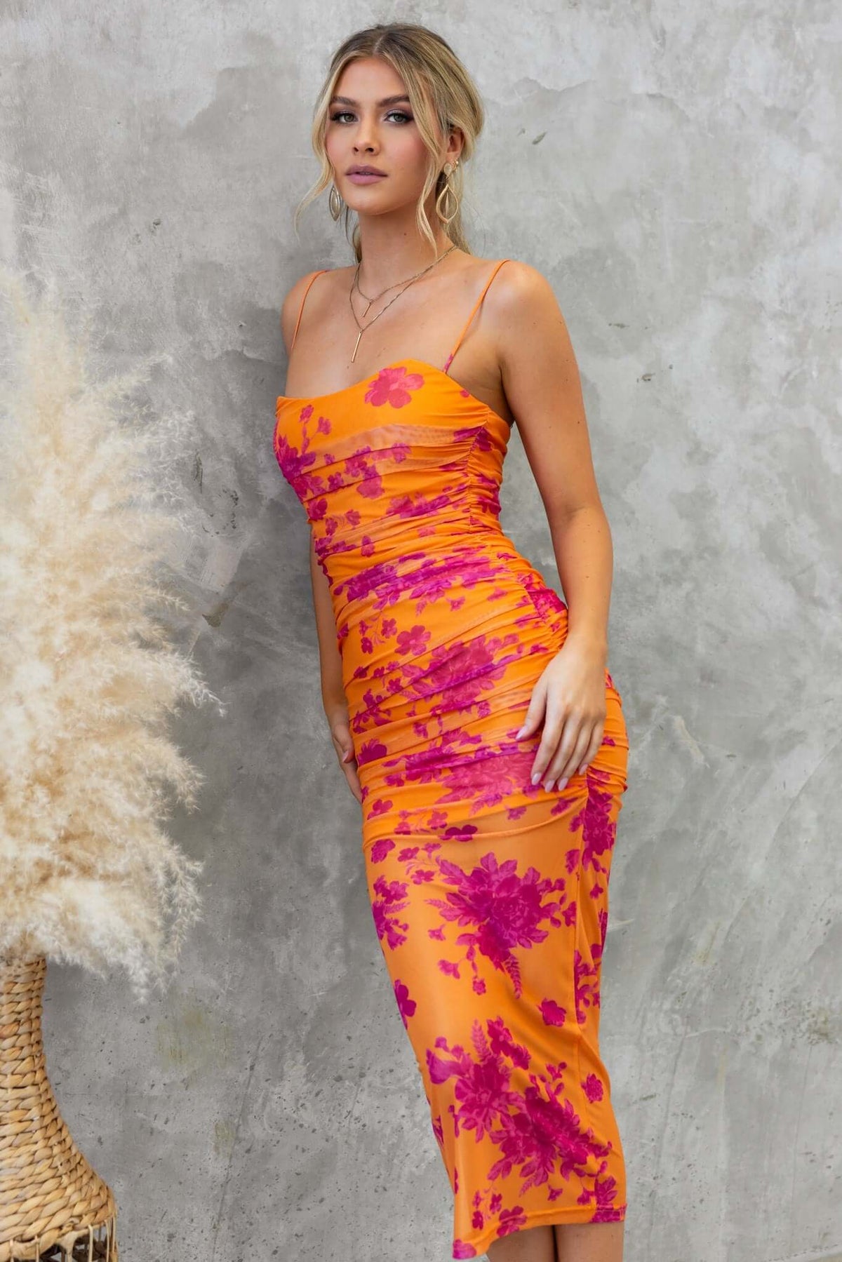 Azriel Midi Dress in orange and pink floral print with ruched sides and adjustable straps, styled against a textured background.