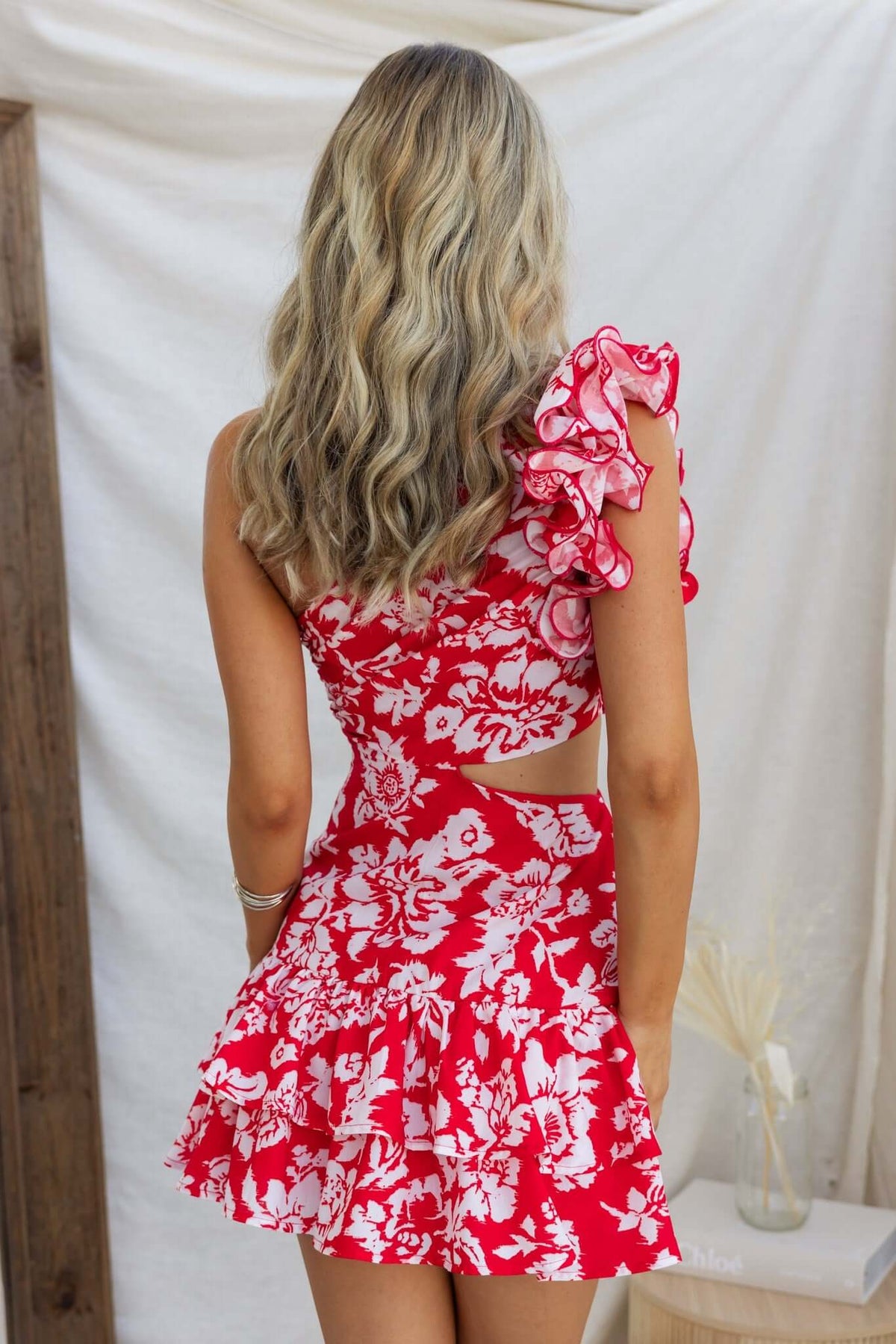 Back view of a woman in a floral red one-shoulder dress with ruffles and cut-out waist detail.