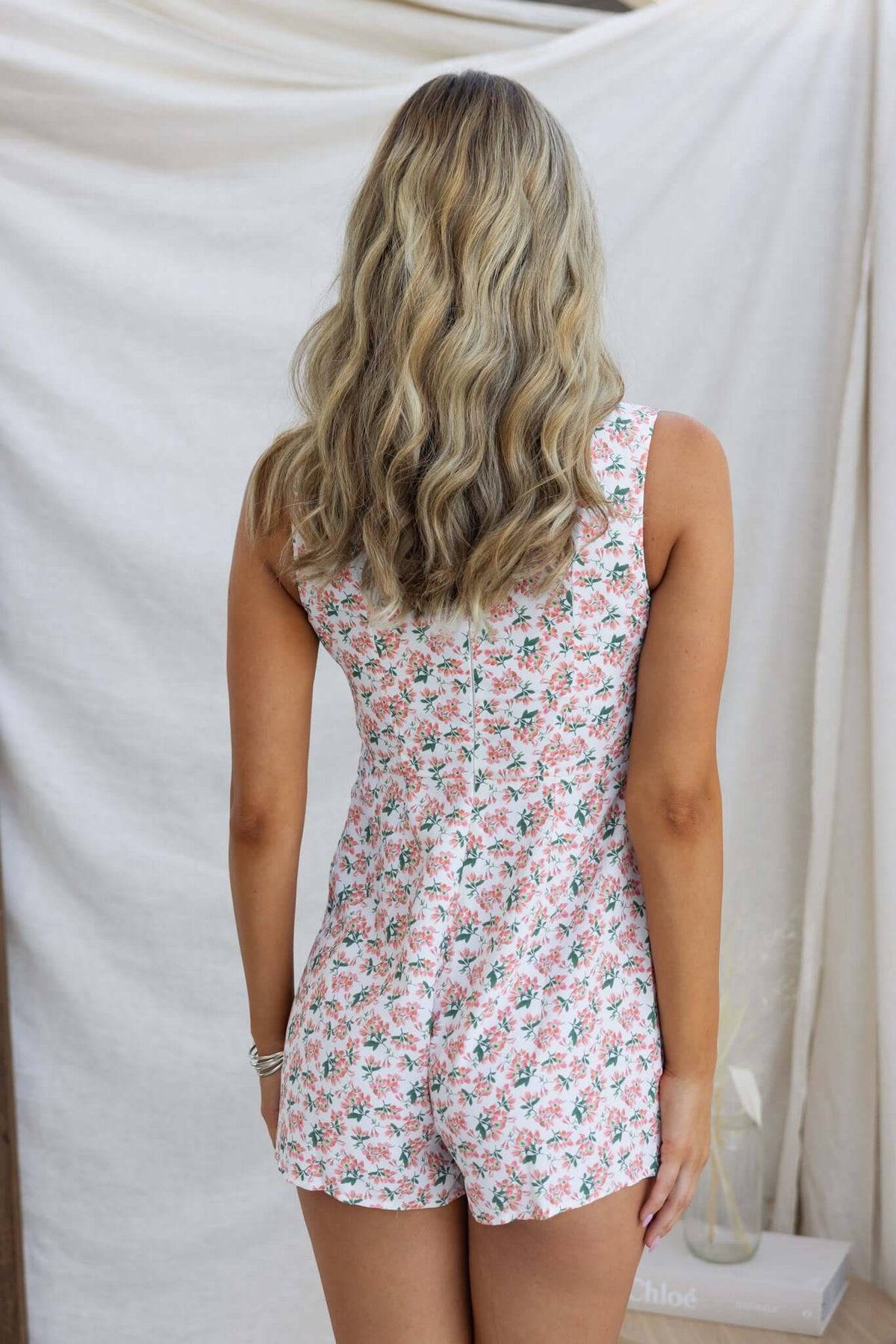 Back view of a woman in a floral Karsyn Playsuit, featuring a V-neckline and button-up design.