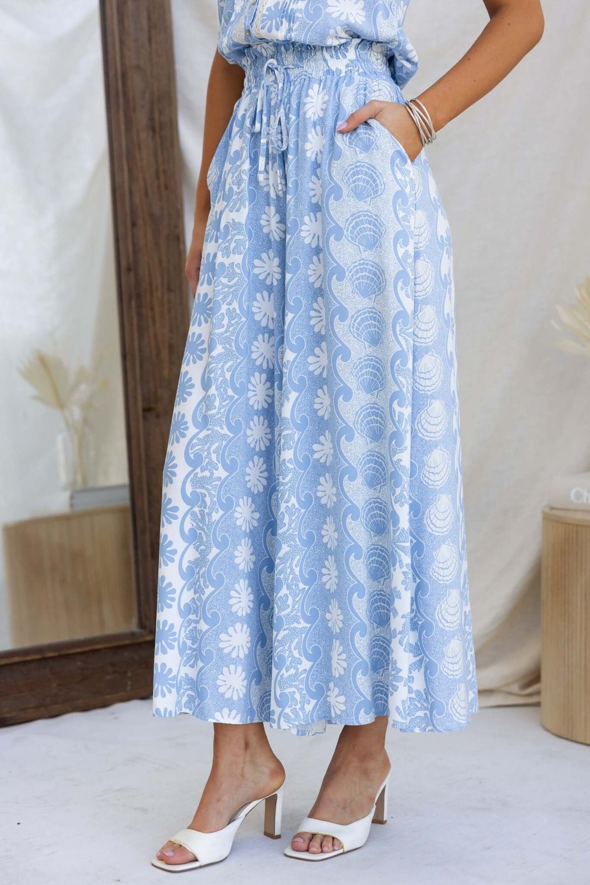 Lunita Pants in light blue with floral pattern, featuring mid-high waist, elastic waistband, and pockets.