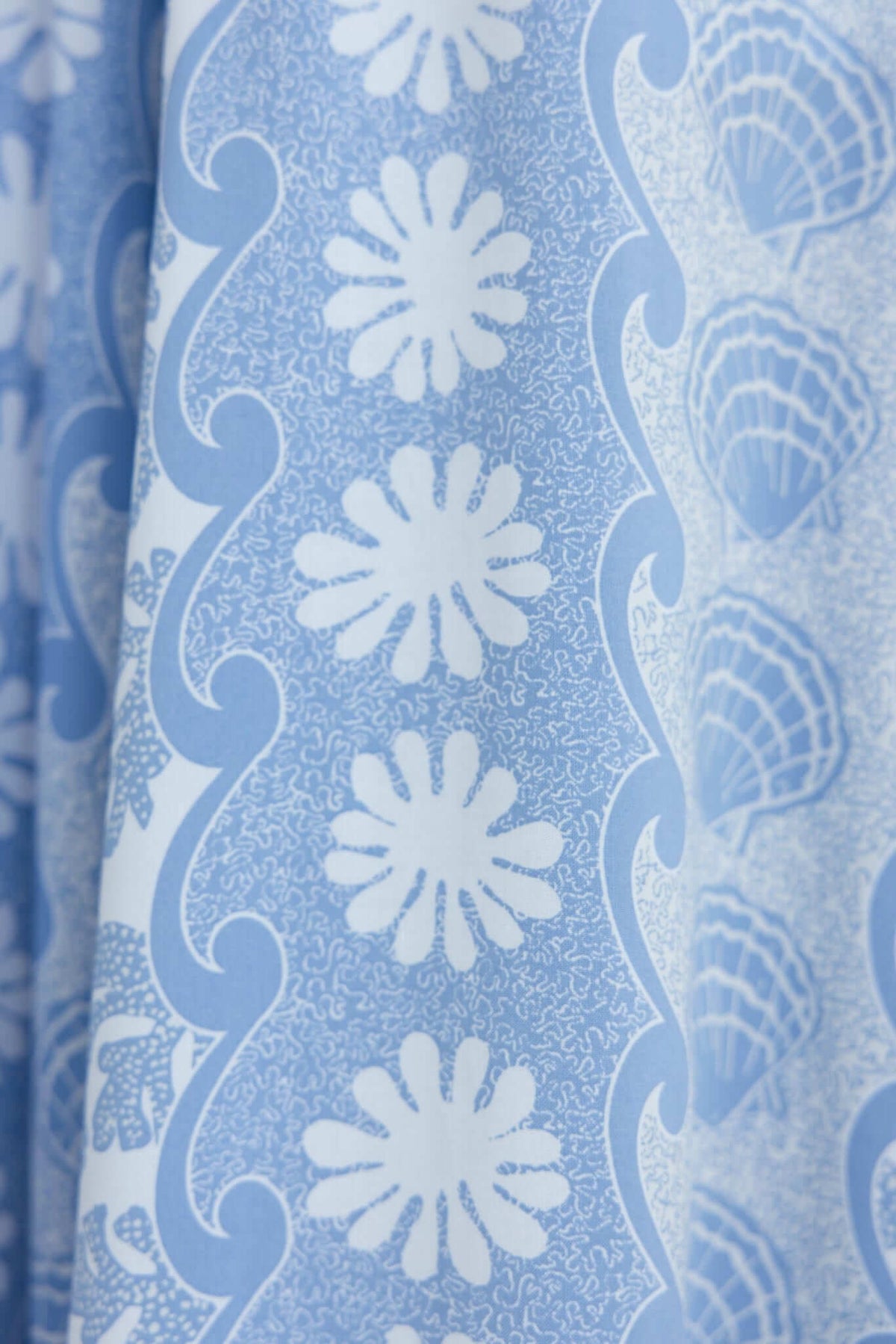Close-up of blue fabric showcasing a floral and shell pattern, ideal for stylish clothing designs.