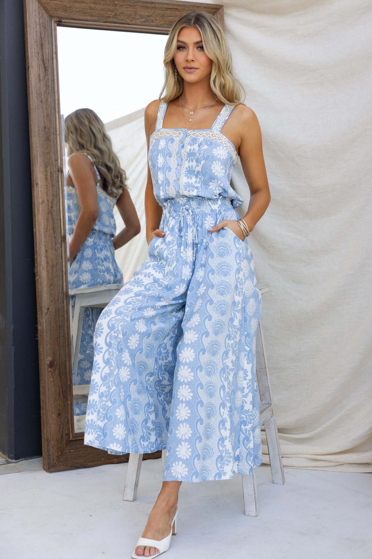 Model wearing Lunita Pants with mid-high waist and pockets in light blue floral print, styled in a mirror setting.
