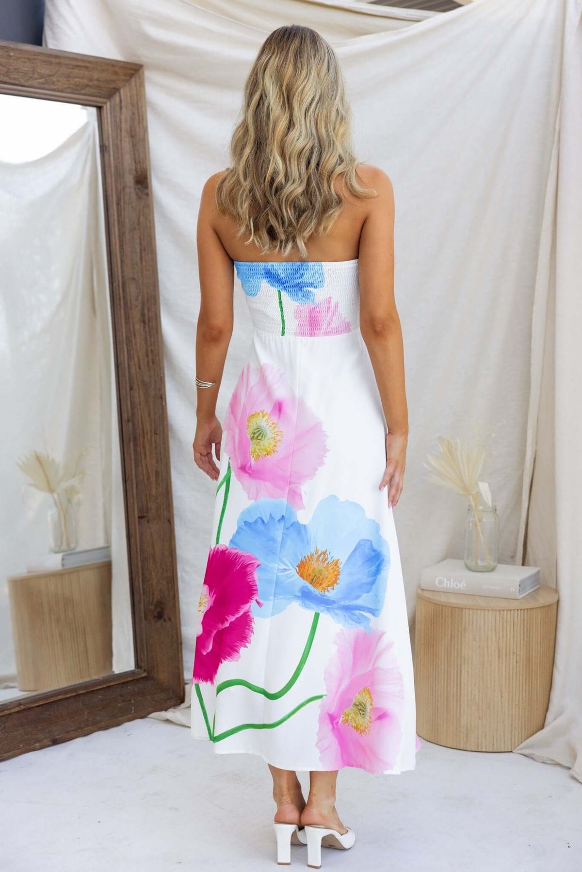 Model wearing Delphina Maxi Dress with floral print, showcasing back design and elegance in a chic setting.