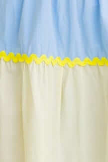 Close-up of a dress featuring a blue top and soft yellow ruffled hem, highlighting its playful color contrast.