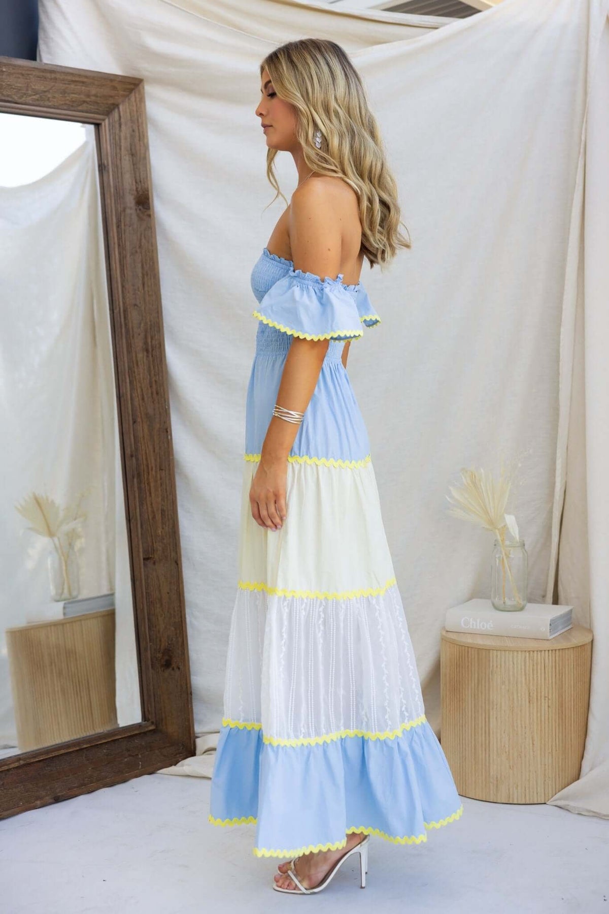 Side view of a woman wearing a light blue and white striped Palmer Maxi Dress with yellow accents and an elastic bodice.