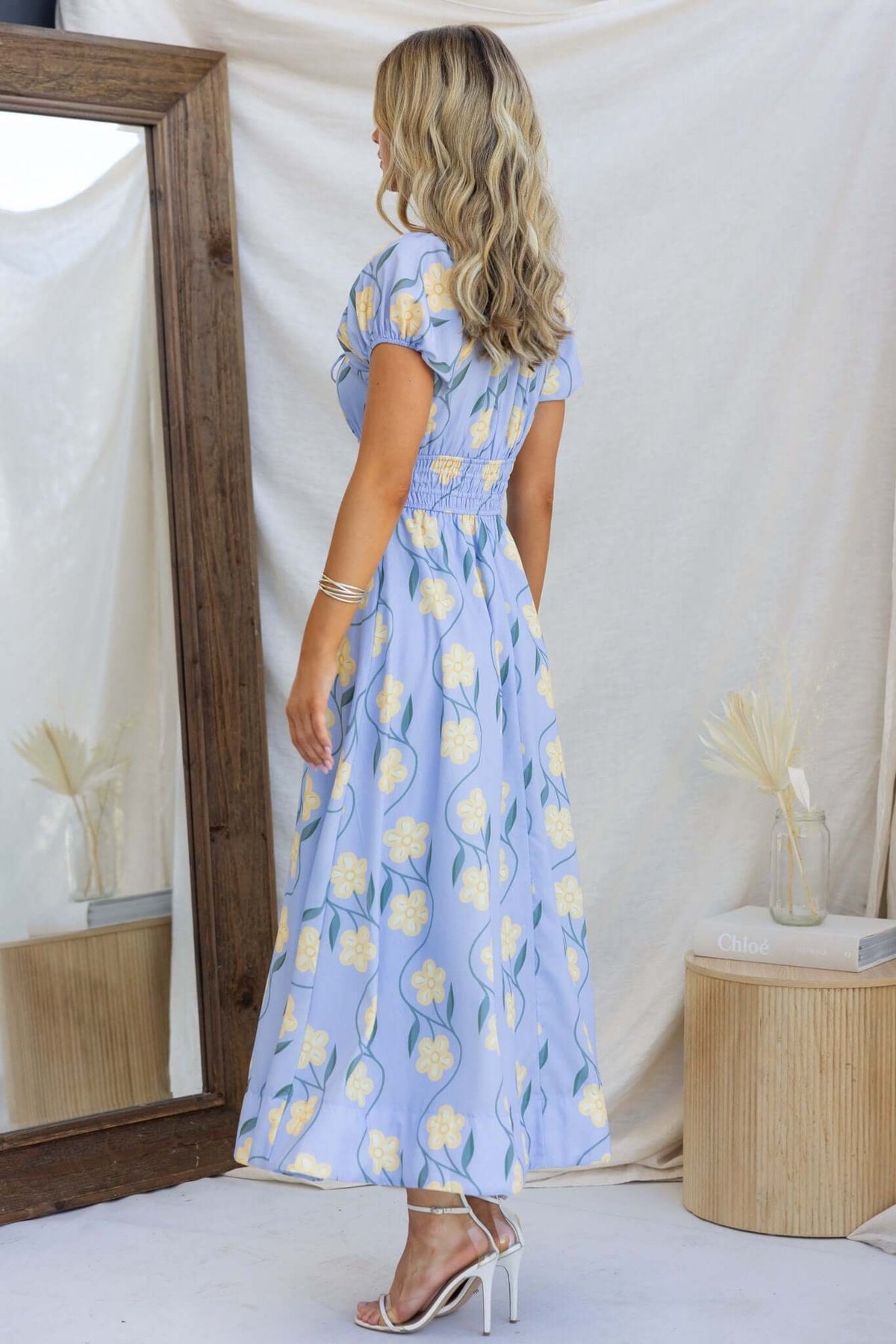 Back view of the Elkhart Maxi Dress featuring floral patterns, an elastic bodice, and a flowy design, styled with heels.