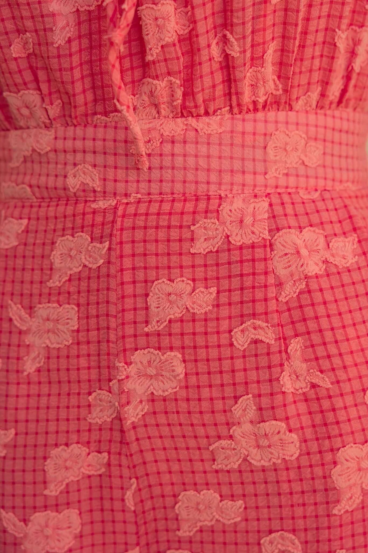 Close-up of pink textured playsuit fabric featuring floral embroidery and checkered pattern.