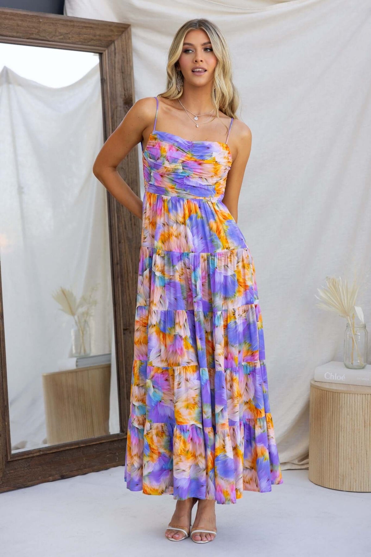 Model wearing Emmelina Maxi Dress in vibrant purple and orange floral print with adjustable straps and flowy skirt.