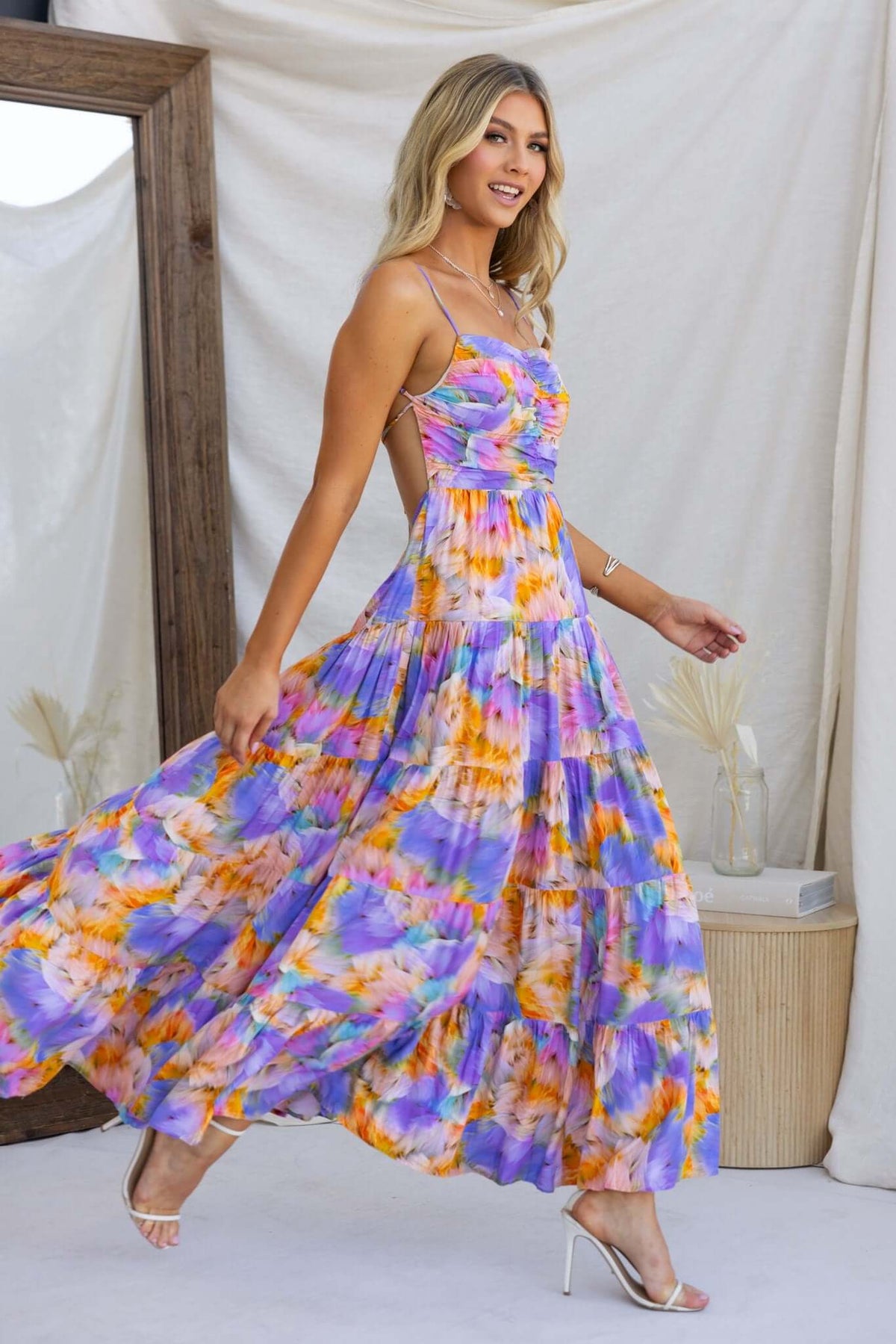 Model wearing Emmelina Maxi Dress in vibrant purple and orange floral print, showcasing adjustable straps and a flowy silhouette.