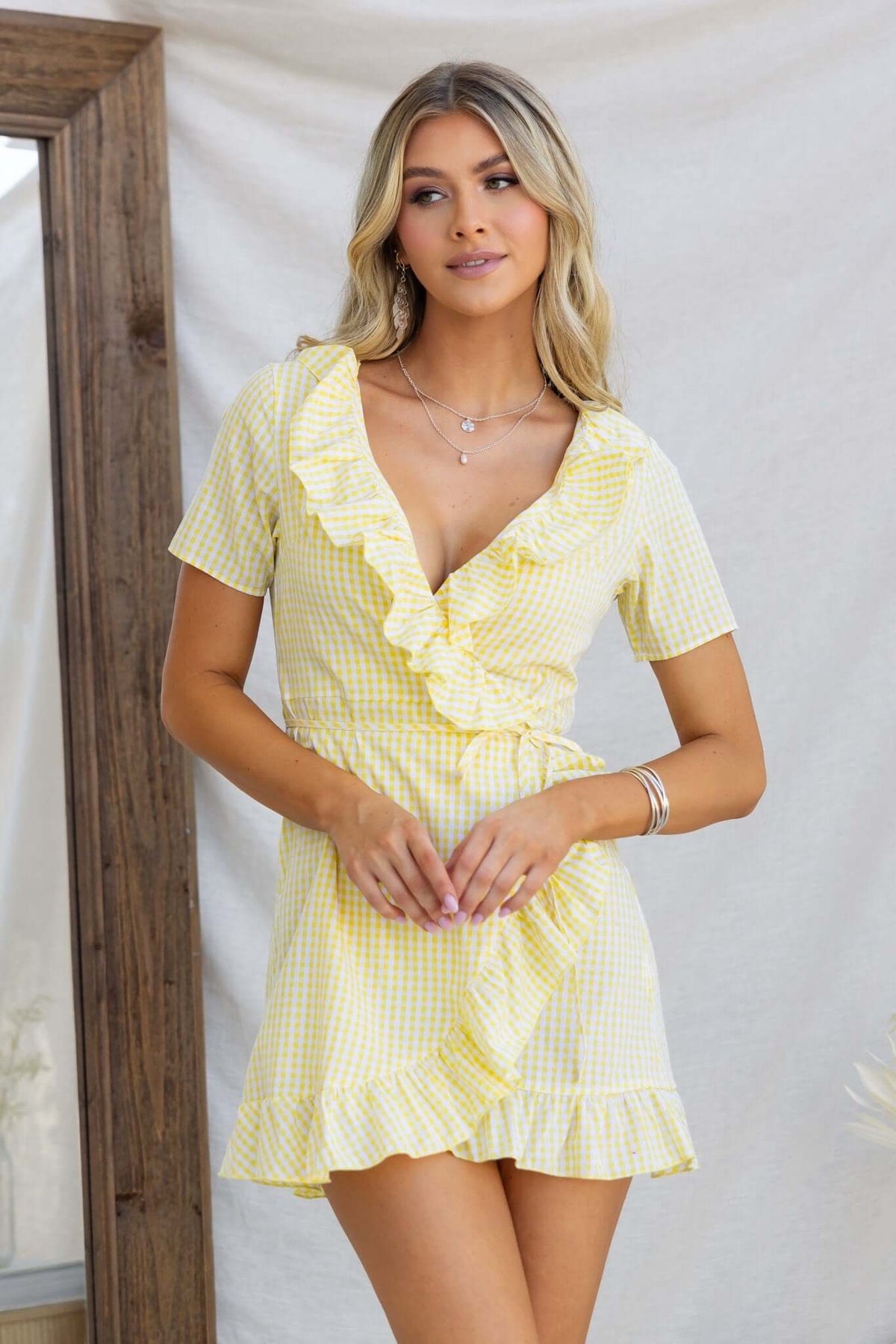 Model wearing a yellow and white checkered May Wrap Dress with a V-neckline and ruffle detailing.
