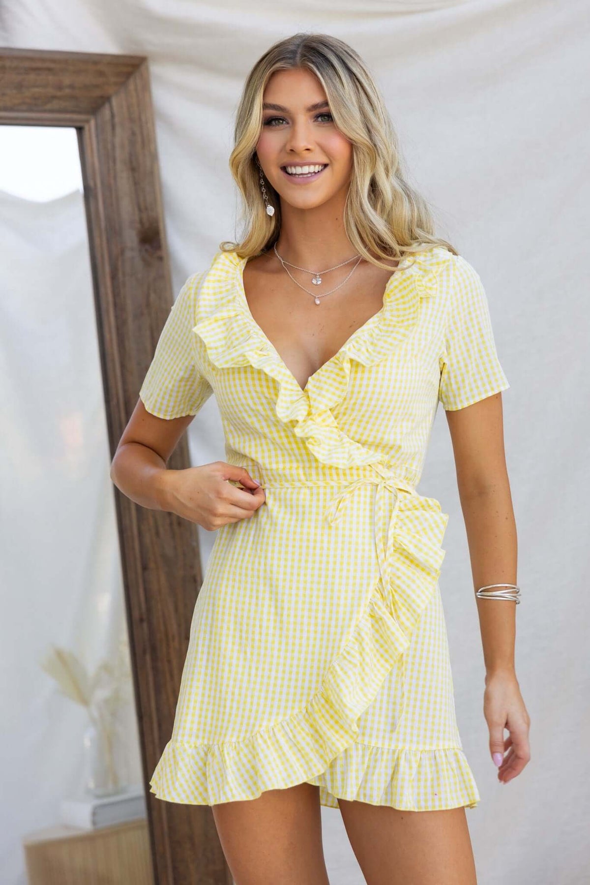 Model wearing a yellow gingham May Wrap Dress with ruffle details and a V-neckline.