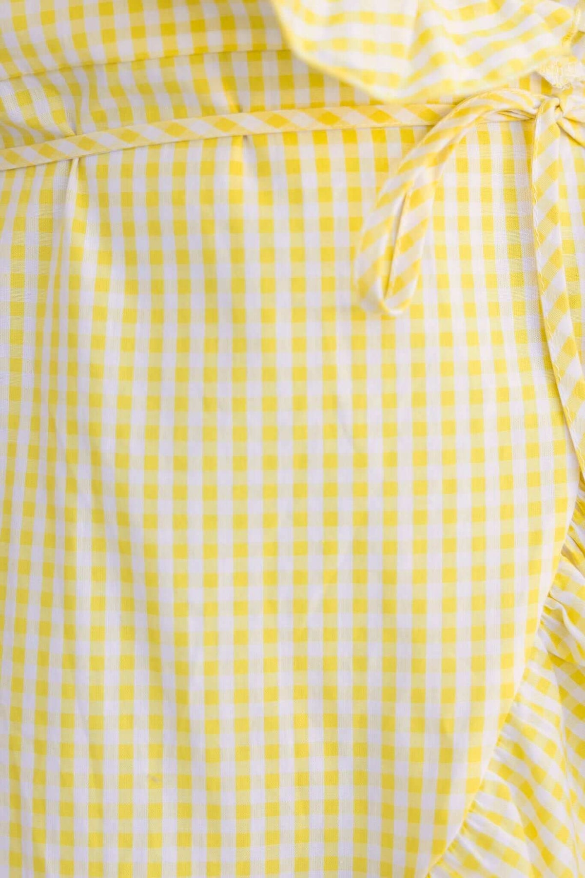 Close-up of yellow gingham pattern on a wrap dress with tie detail, showcasing the fabric texture and design.
