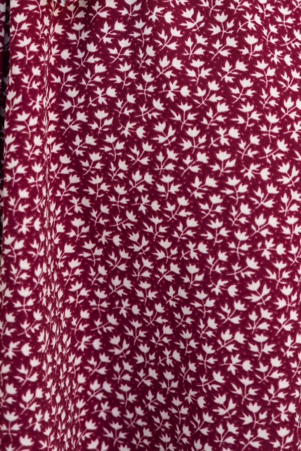 Close-up of burgundy fabric with white leaf print, highlighting floral pattern for Farsan Dress.
