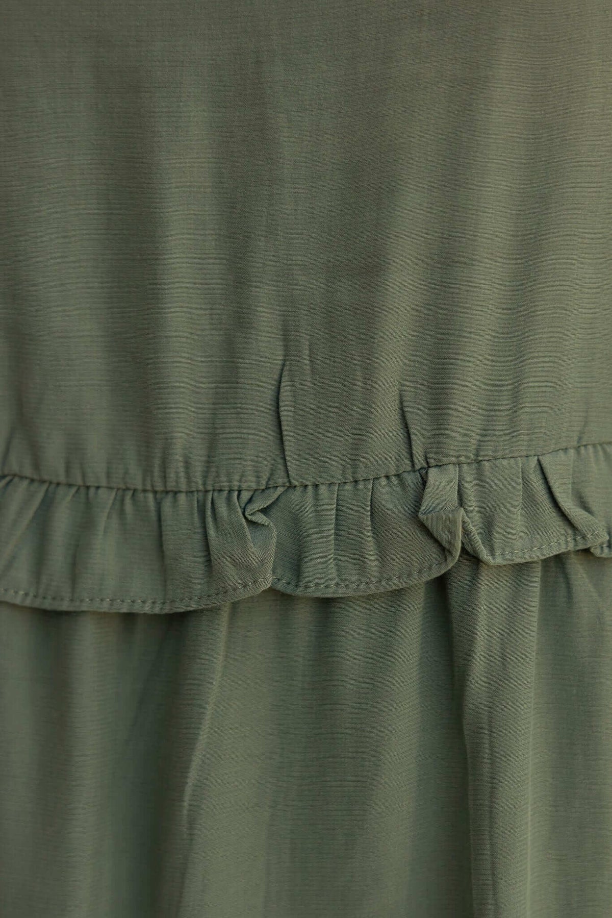 Close-up of the ruffled hem detail on the Bourne Dress in olive green fabric, showcasing its stylish texture.