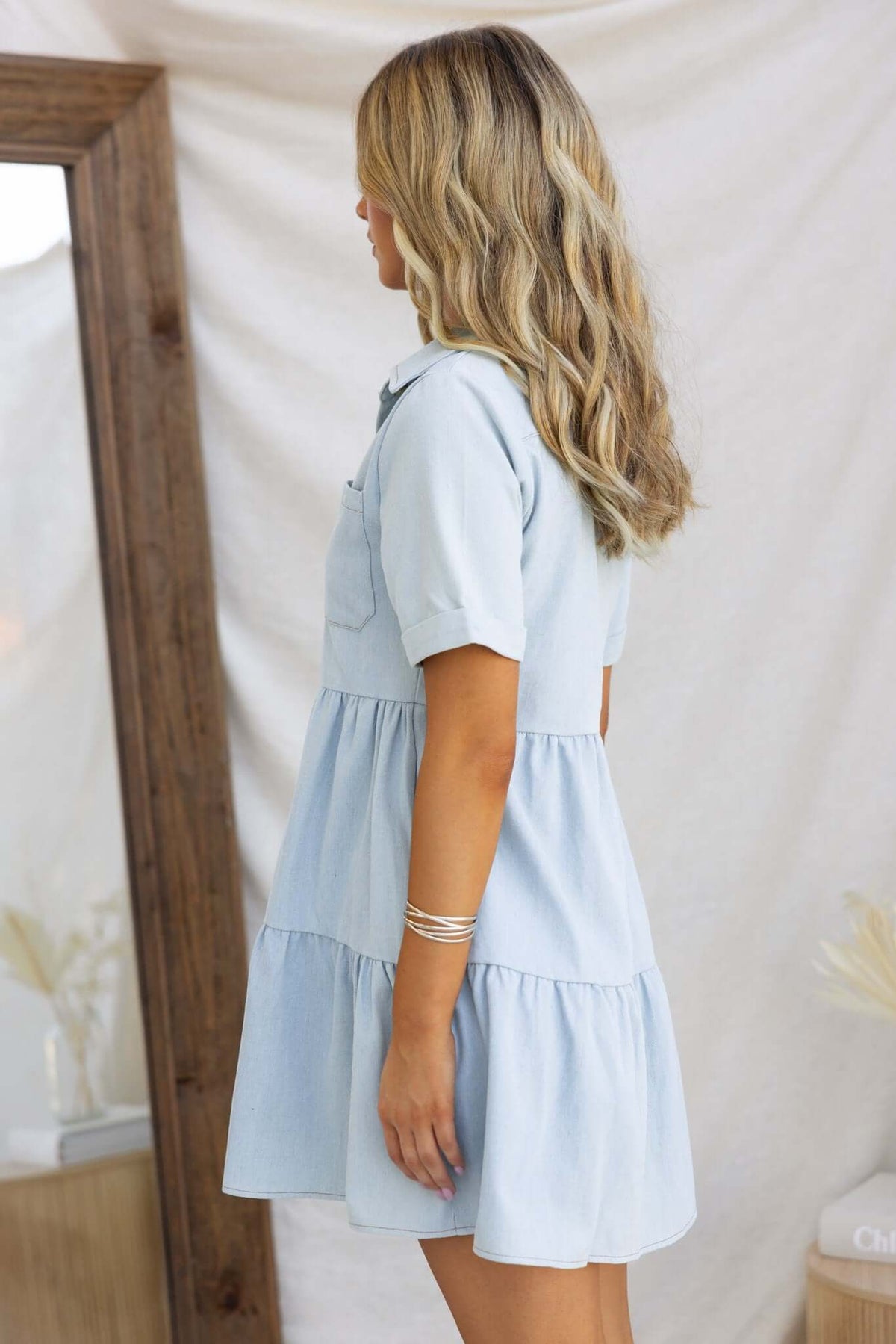Side view of a Jessy Denim Dress featuring a collar, button-up front, and pockets, styled on a model.