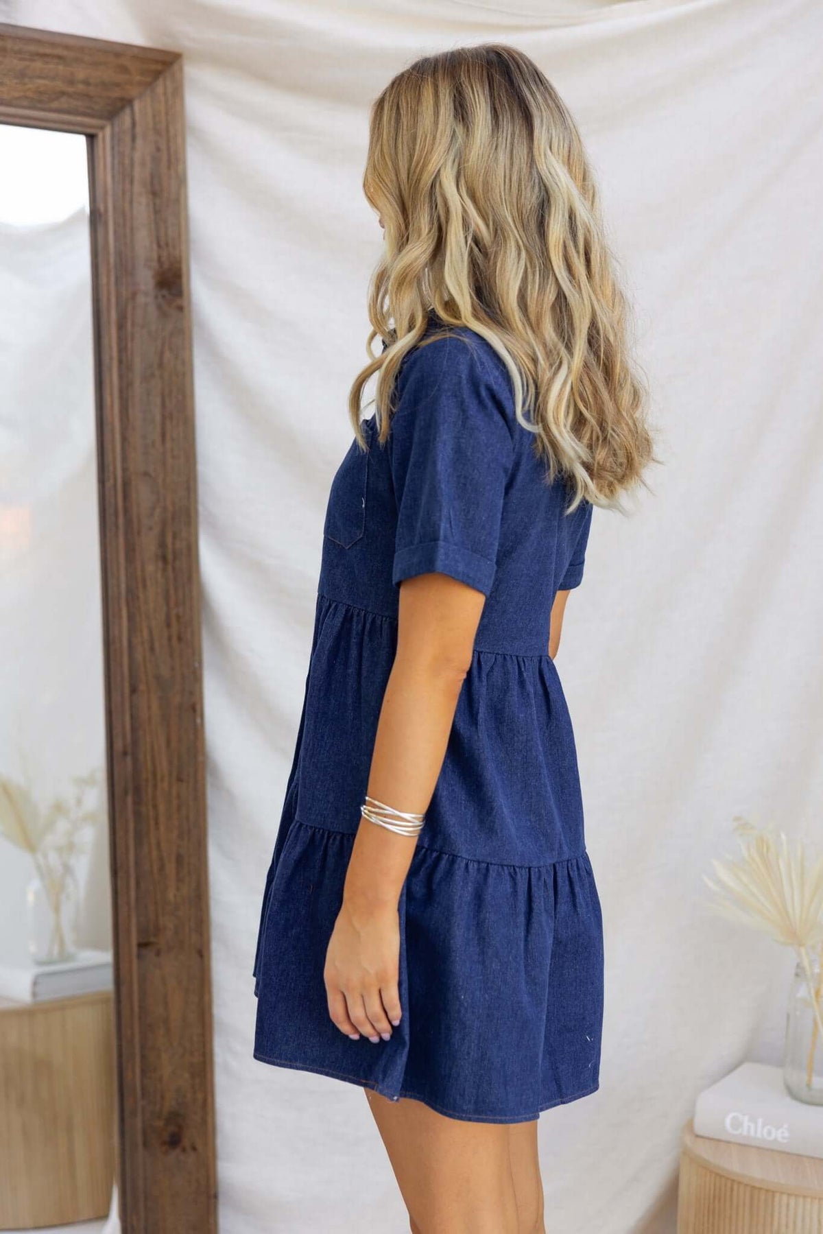 Side view of a woman wearing a Jessy Denim Dress with short sleeves and tiered design, showcasing its stylish silhouette.