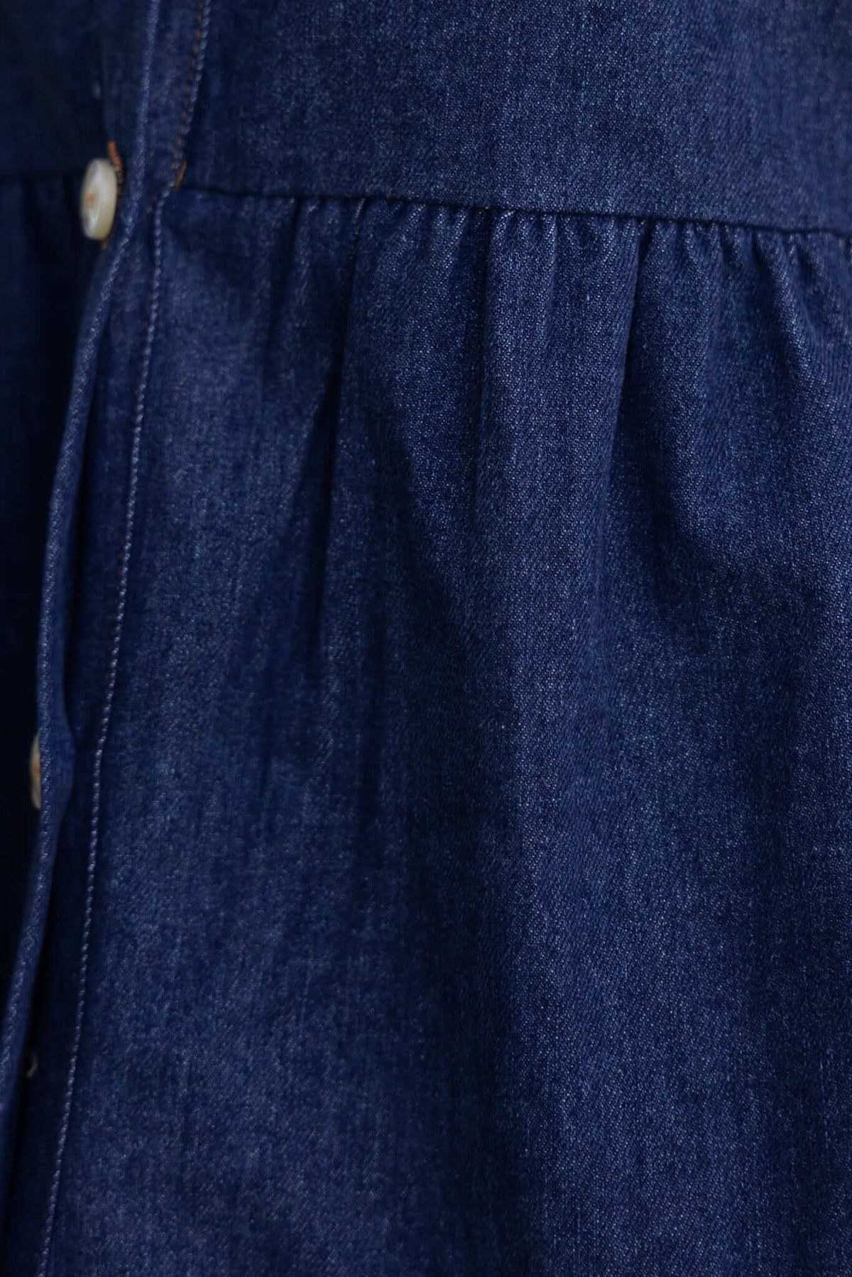 Close-up of Jessy Denim Dress fabric showing button detail and gathered waist.