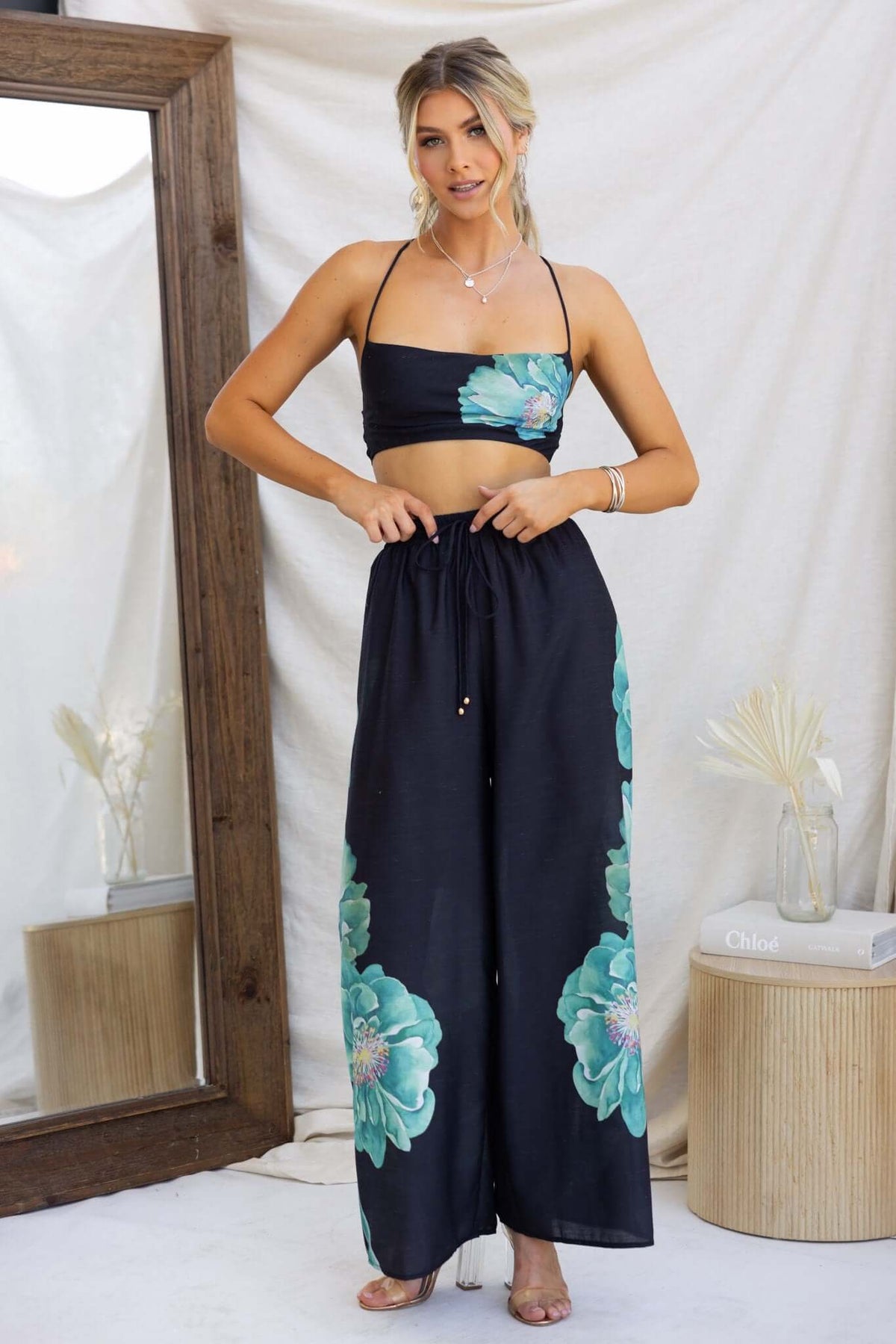 Model wearing Faly Pants, black wide-leg pants with floral print, paired with a matching crop top.
