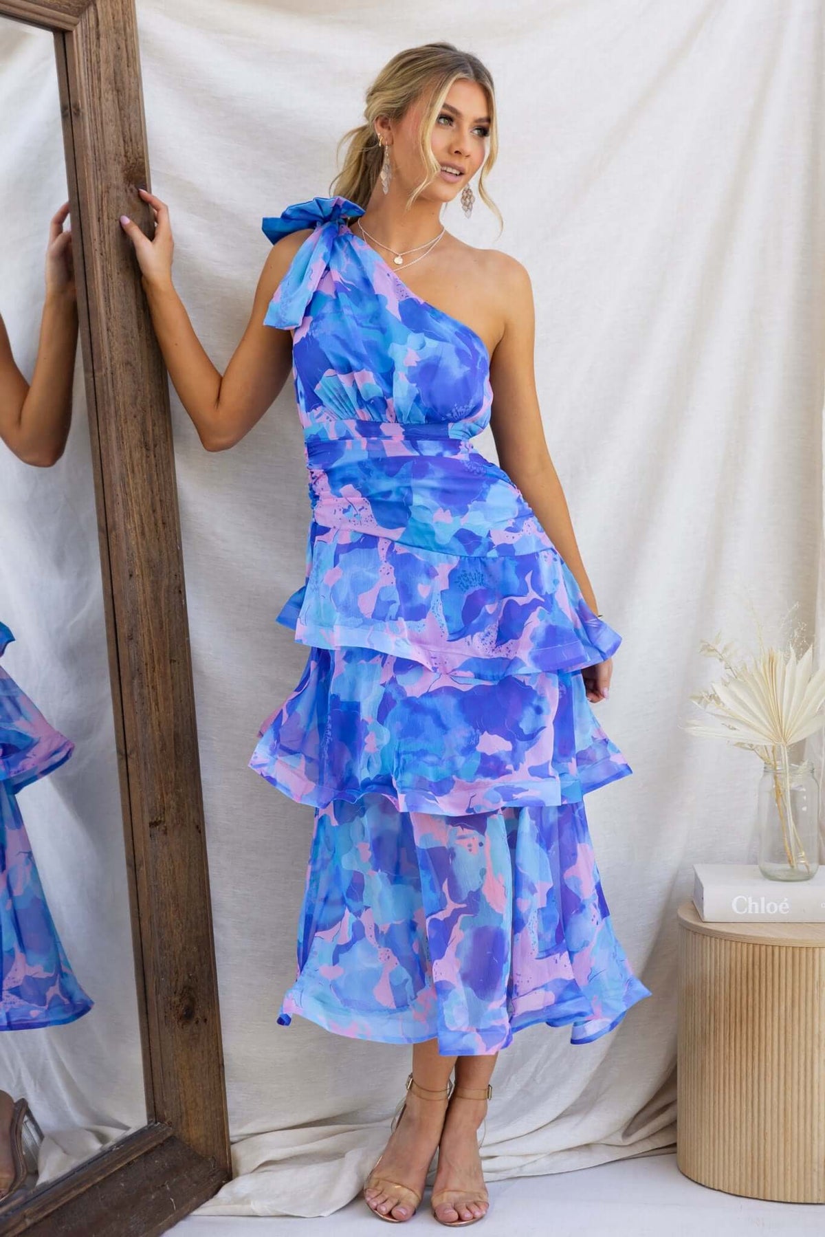 Model wearing a vibrant blue and pink Sherbert Midi Dress featuring a one-shoulder neckline and tiered ruffle hem.