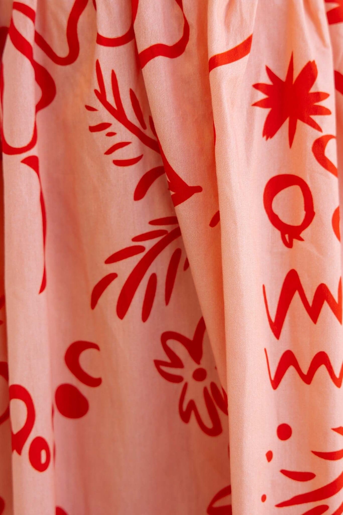 Close-up of the Missie Dress, featuring a pink fabric adorned with vibrant red patterns and floral designs.