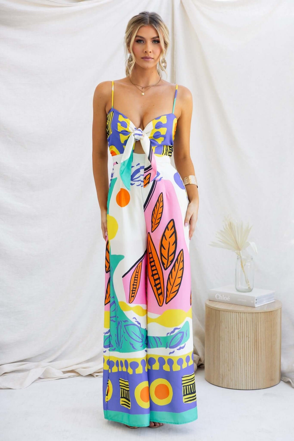 Stylish woman wearing a multi-colour print jumpsuit with adjustable straps and a tie at the bust.